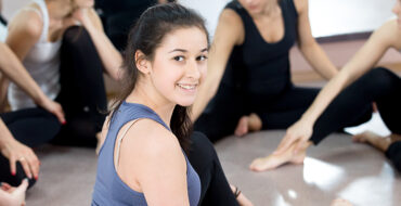 Group of happy sporty young women chatting on break in sports gy Group of sporty young female friends chatting, resting, on break after exercises in sports club, gym class. Focus on smiling teenage female athlete in color sportswear